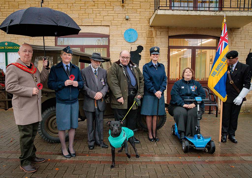 The Mayor of Carterton (left) stands with Station Commander, Group Captain Kate Macartney, two gentlemen Veterans, one with a dog on a leash, Station Warrant Officer Sim and a lady on a mobility scooter, in front of a WWII Military Jeep, with the Town Hall in the background.